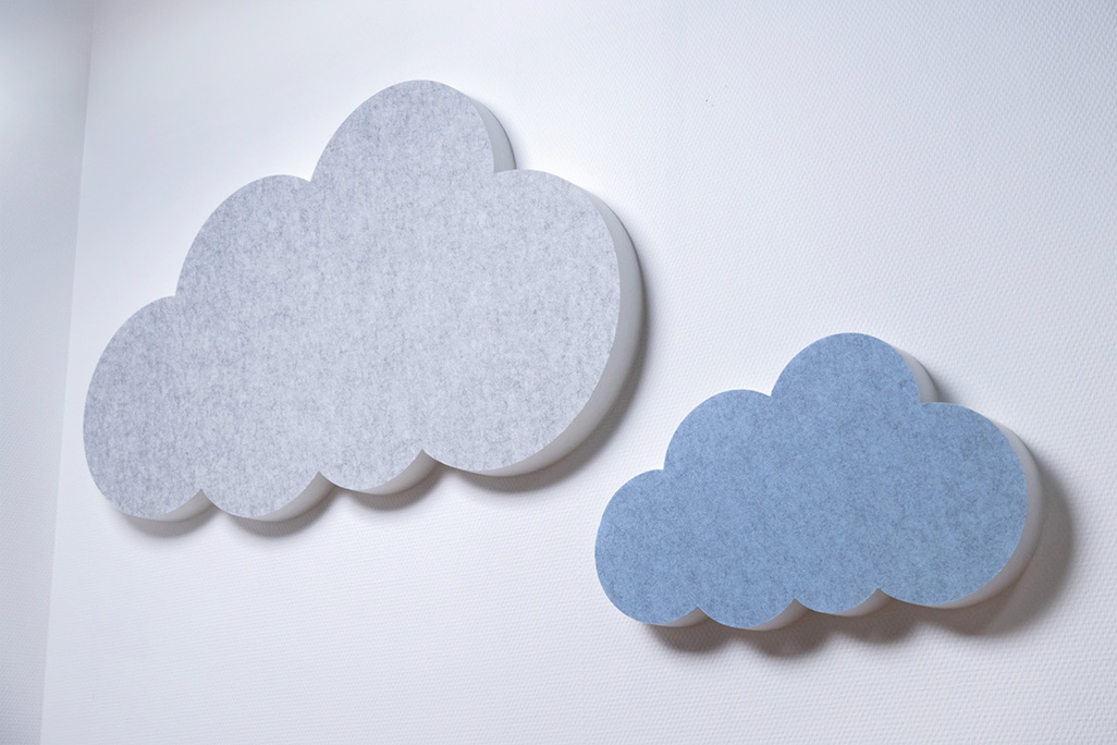 Two sound absorbers in the shape of a cloud in blue and light gray on a white wall.